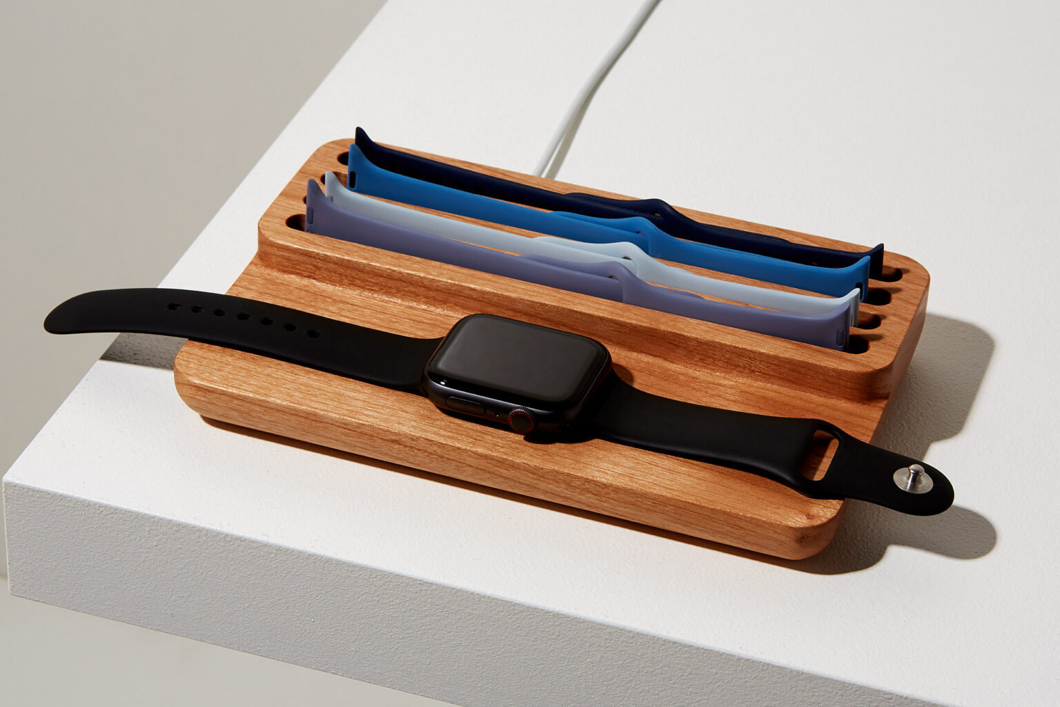 Anden Watch Valet in oak holding an Apple Watch with black and blue spare straps
